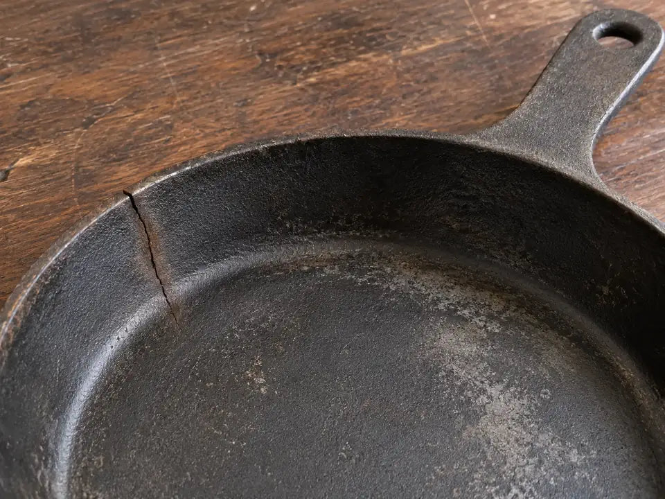 Poêle en fonte fêlée : une fine fêlure part du bord d'une vieille poêle en fonte et descend vers l'intérieur