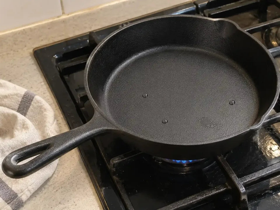 Poêle en fonte neuve posée sur une petite flamme de gazinière pour sécher les dernières gouttes d'eau après son premier lavage, un torchon à côté