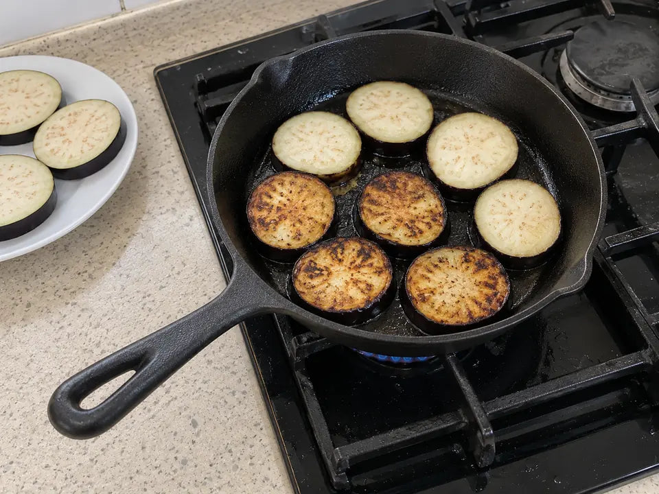 Premières cuissons dans une poêle en fonte remise à neuf : des tranches d'aubergine dorent dans un peu d'huile, sur le gaz