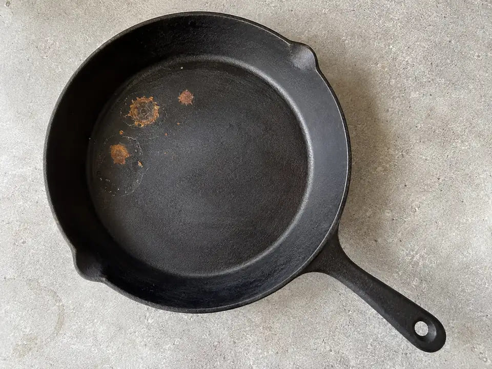 Poêle en fonte rouillée : quelques points de rouille orange et des traces d'eau séchée sur la surface de cuisson d'une poêle noire