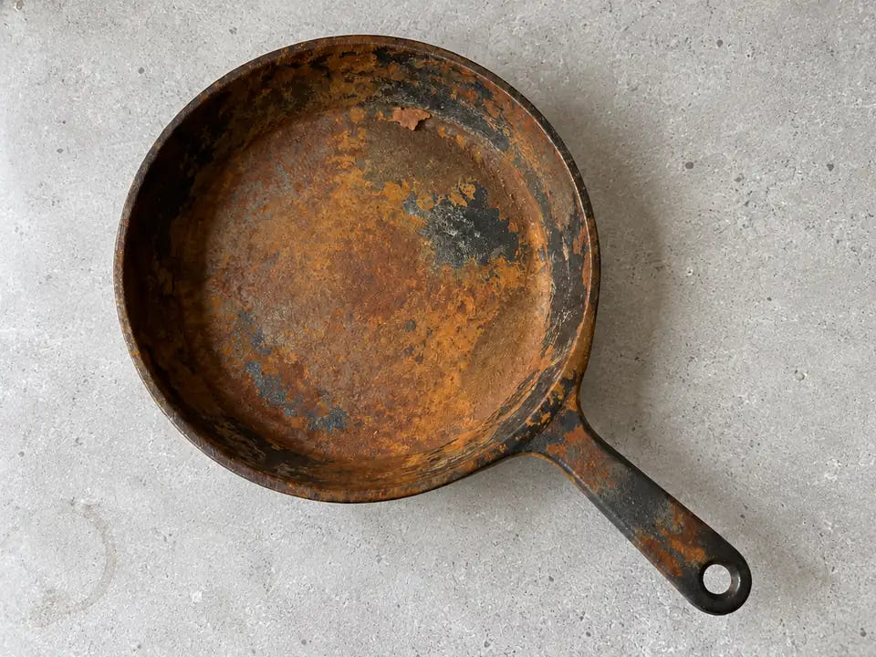 Poêle en fonte rouillée de partout : une rouille orange et brune couvre toute la surface de cuisson, les bords et le manche d'une vieille poêle
