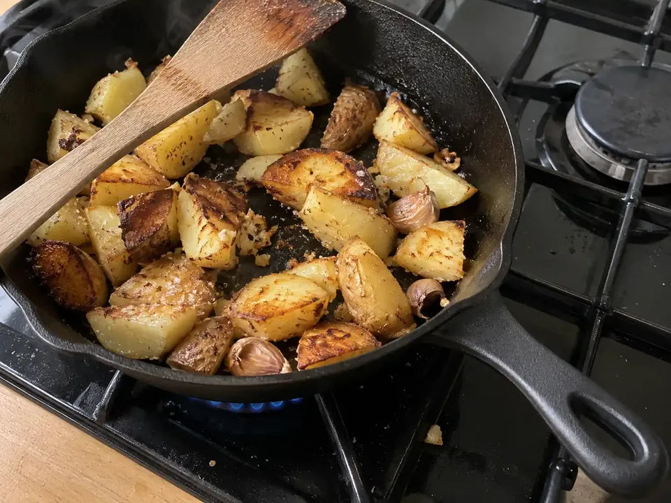 Pommes de terre sautées et gousses d'ail qui dorent directement sur la surface de cuisson d'une poêle en fonte naturelle sans revêtement, sur une gazinière allumée