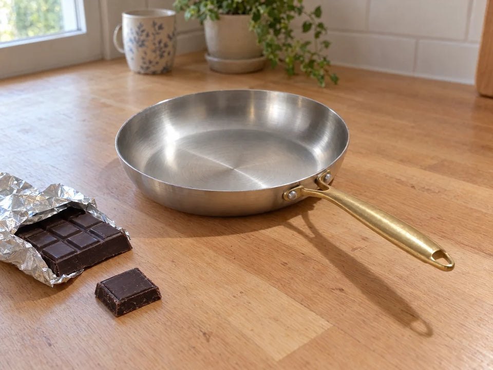 Chocolat noir riche en nickel posé à côté d'une poêle en inox 18/10 sur un plan de travail en bois