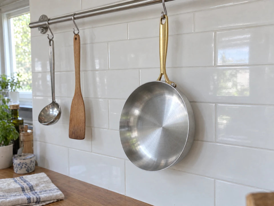 Poêle en inox sans culottage, rangée propre et sèche sans huile, suspendue par son manche doré à une barre de cuisine