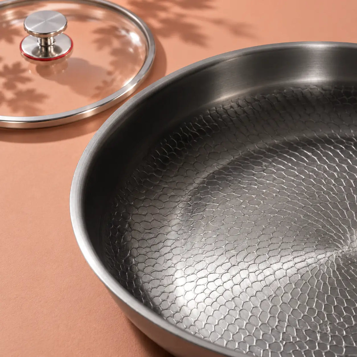 Gros plan sur la surface de cuisson texturée de la poêle en titane 28 cm avec couvercle, le couvercle en verre posé derrière