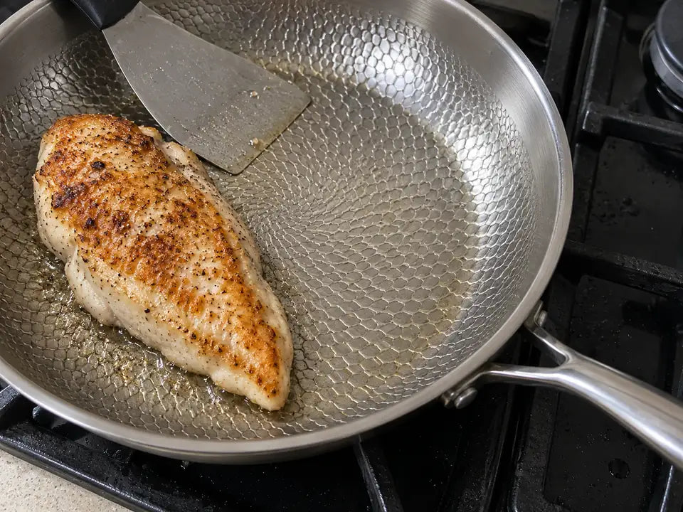Blanc de poulet doré qui vient d'être retourné dans une poêle en titane martelé, sans laisser de morceau accroché