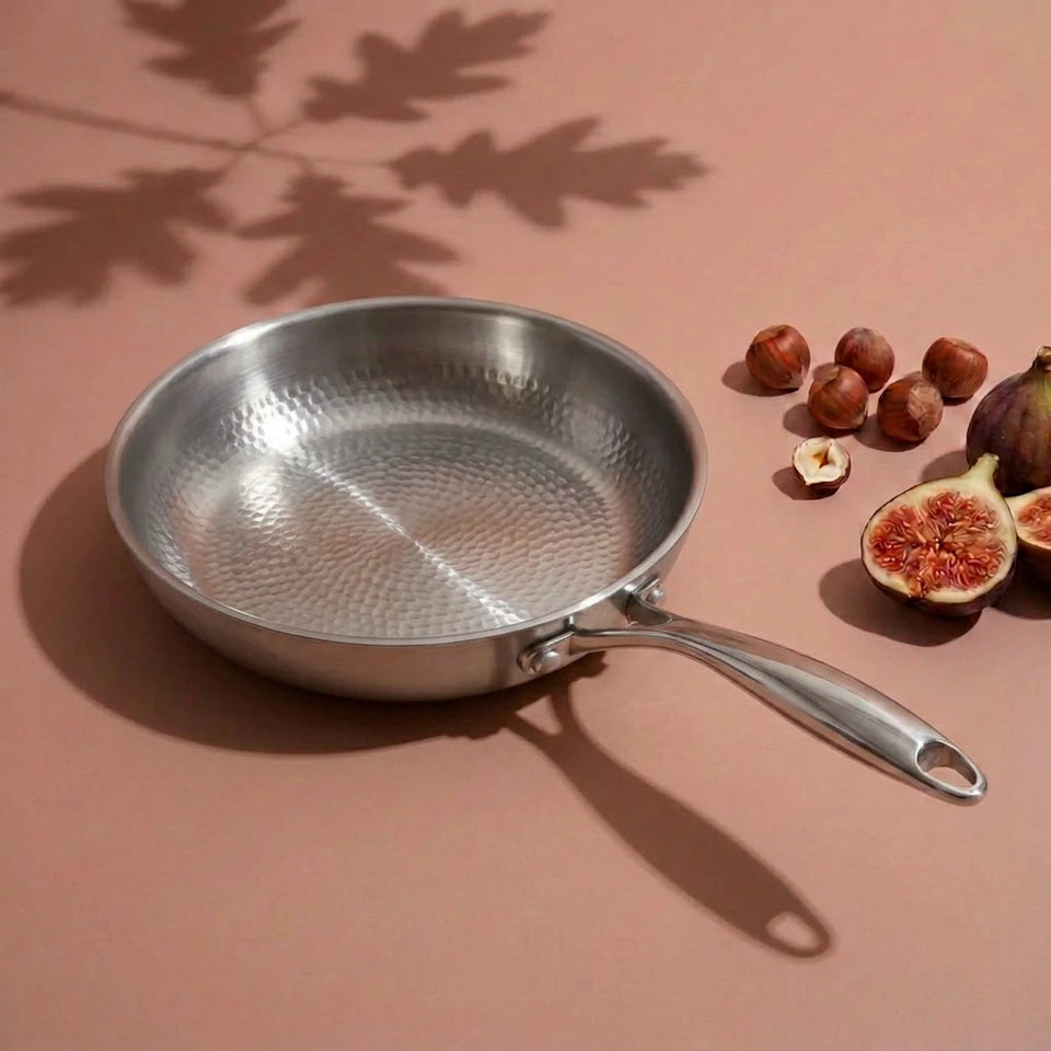 Poêle en titane martelé 28 cm vue de dessus, sa surface alvéolée à côté de figues et de noisettes