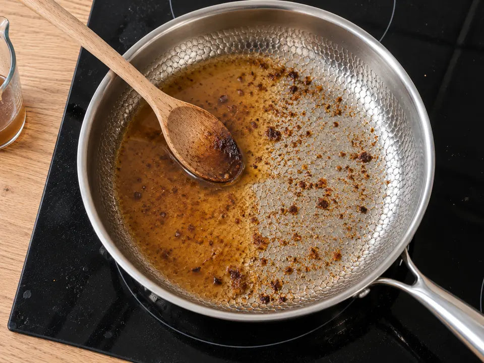 Sucs de cuisson dans une poêle en titane martelé : un peu de bouillon versé dessus et une cuillère en bois pour les décoller
