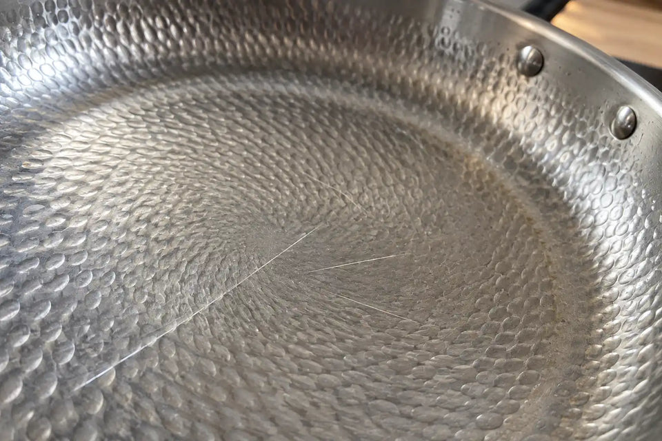 Surface martelée d'une poêle en titane avec quelques fines rayures d'ustensile, le même métal gris dessous