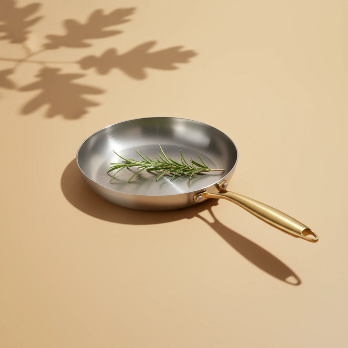 Poêle induction 24 cm vue de dessus, un brin de romarin frais posé sur sa surface de cuisson brossée