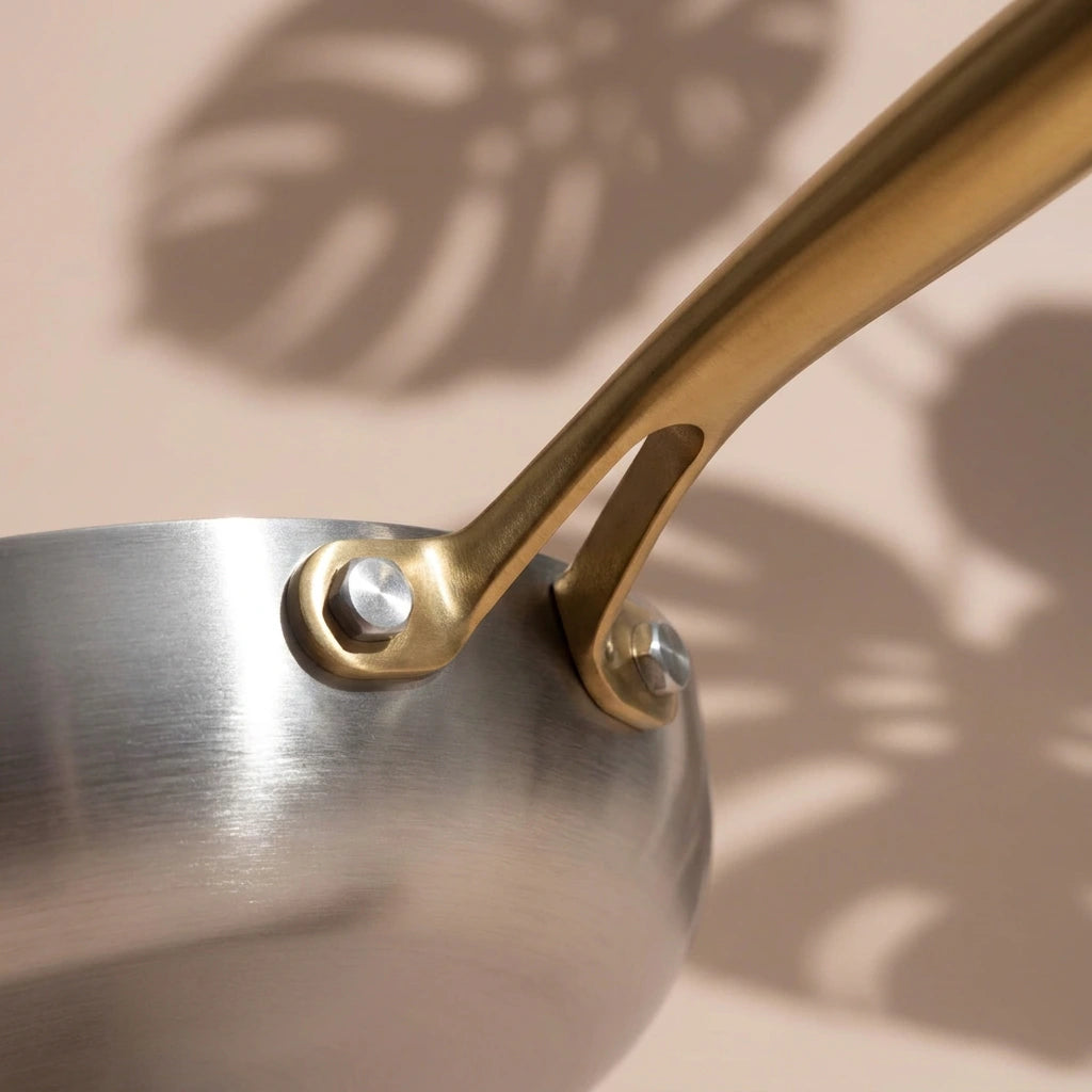 Rivets du manche doré de la poêle induction 30 cm vus de très près, posés contre la paroi brossée