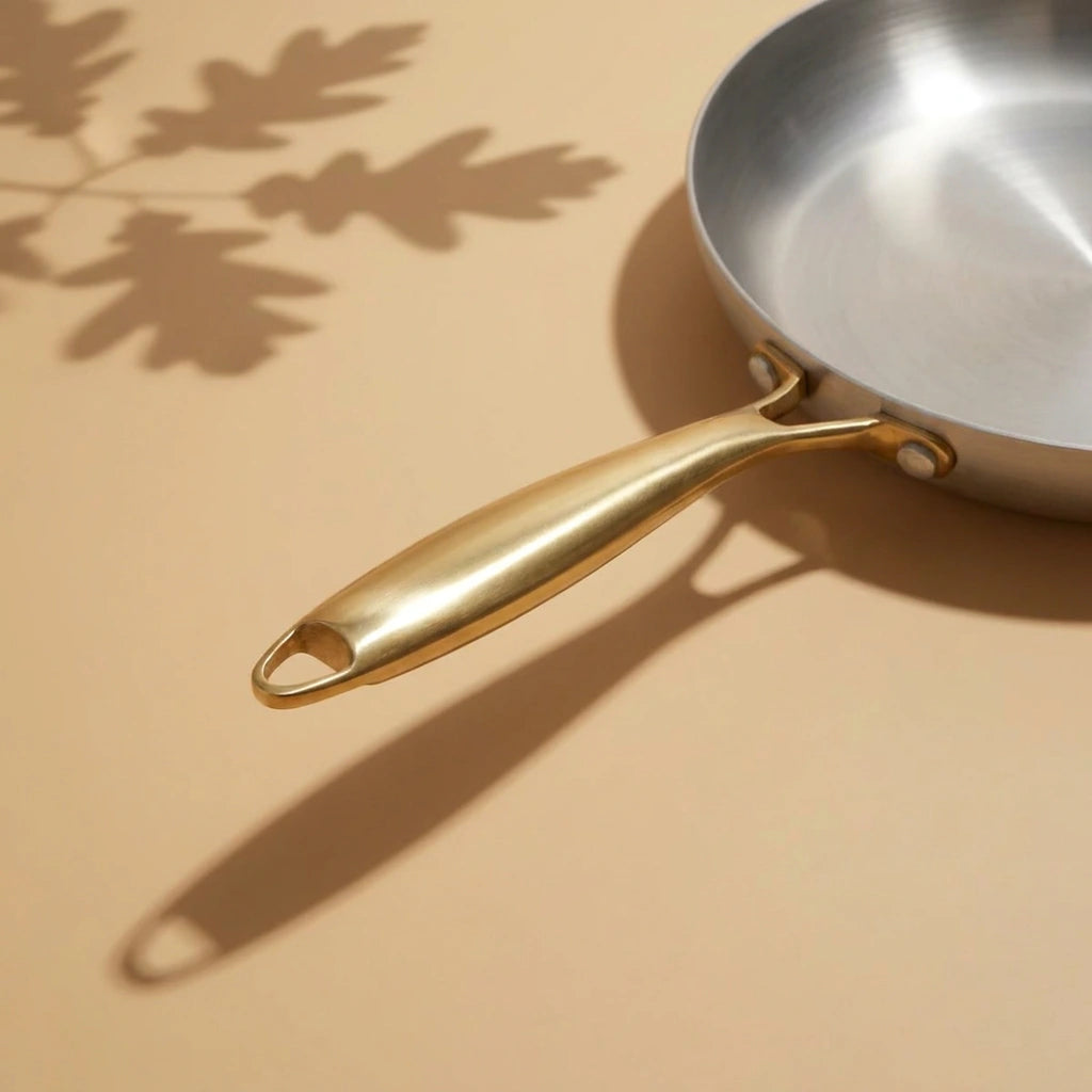 Manche doré de la poêle induction 30 cm en entier, son ombre portée sur le plan de travail