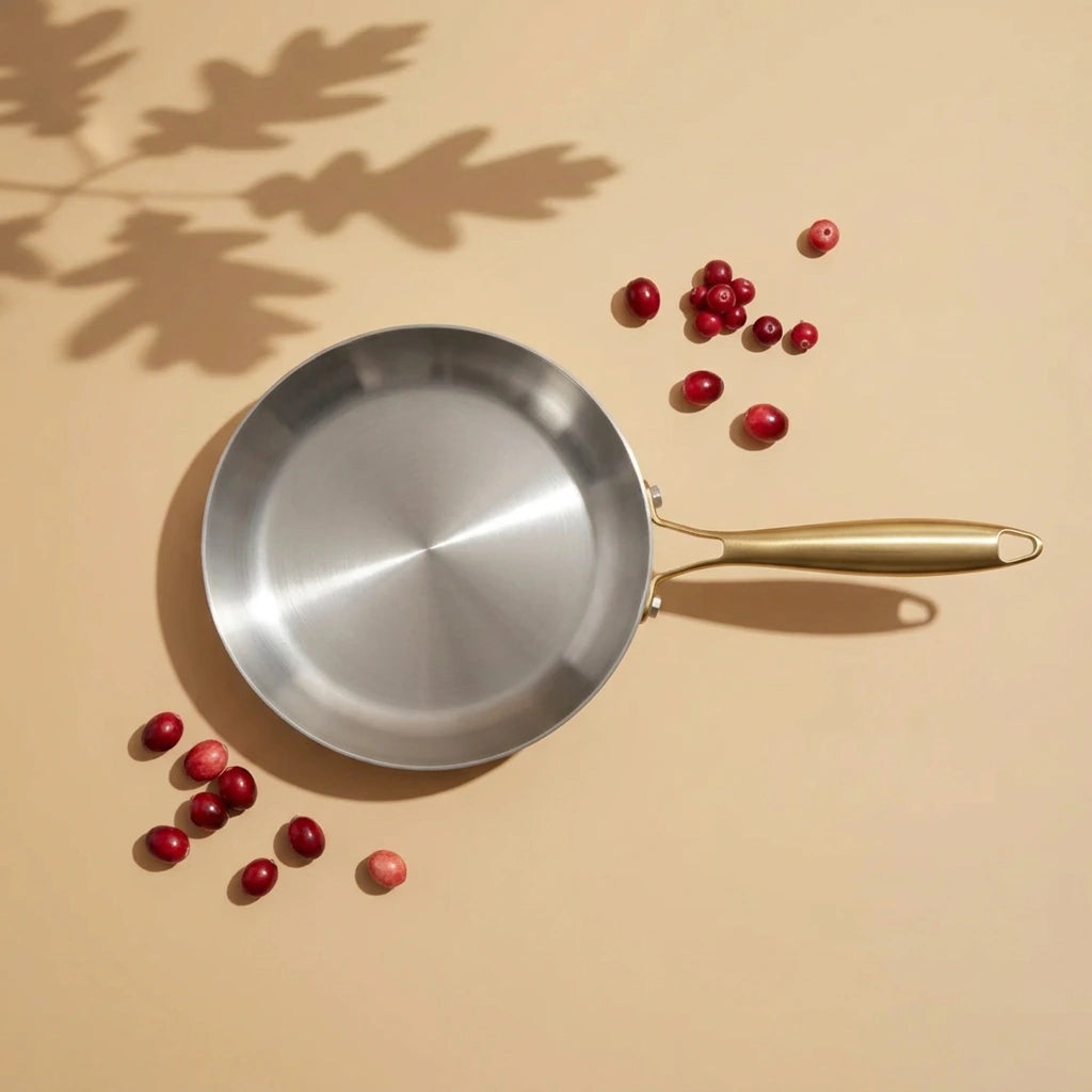 Poêle induction 30 cm vue de dessus, sa très large surface de cuisson brossée, des baies roses éparpillées à côté
