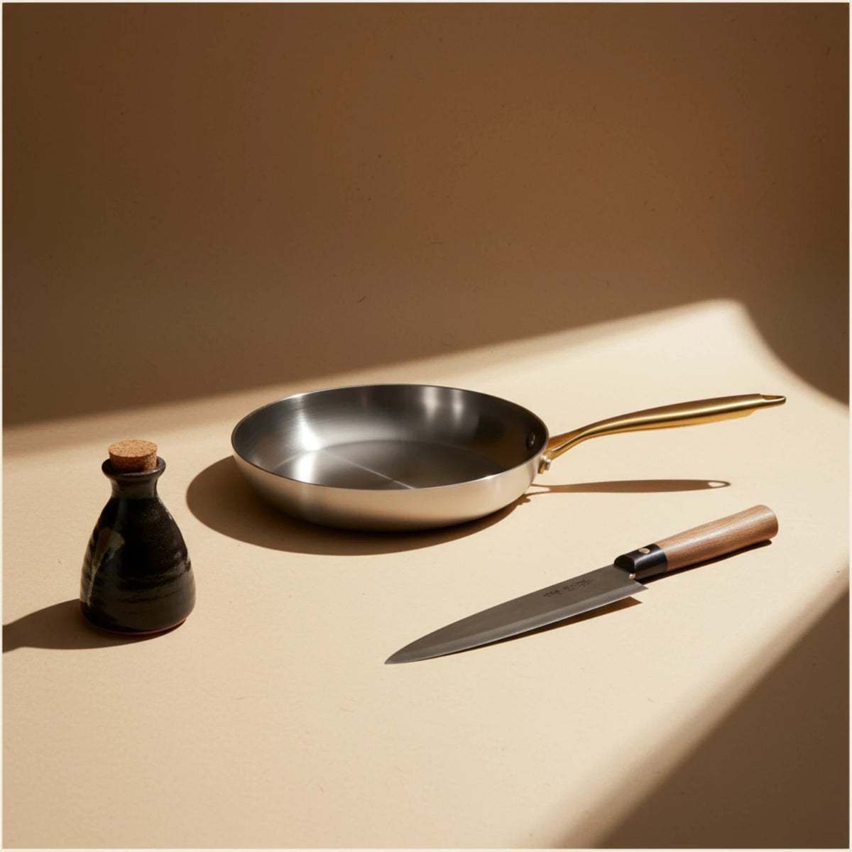 Poêle inox 26 cm : présentation sur fond beige avec un couteau et une bouteille de sauce.