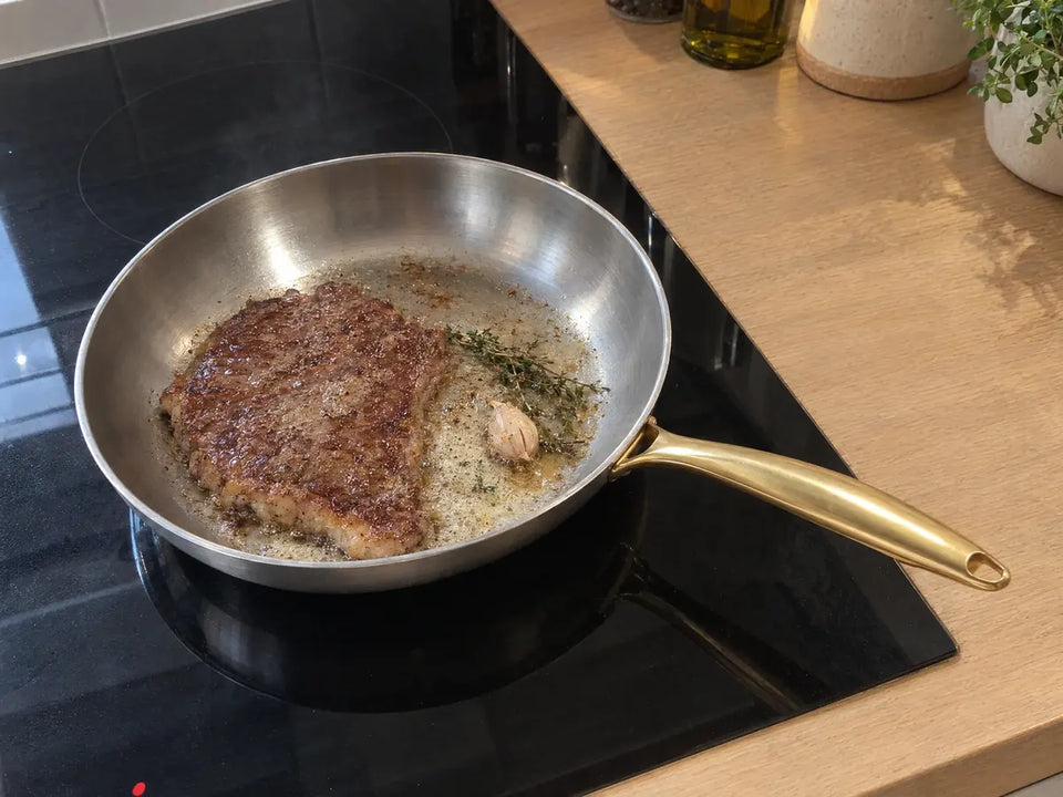 Entrecôte saisie dans une poêle inox 28 cm sur une plaque à induction, avec du beurre, de l'ail et du thym