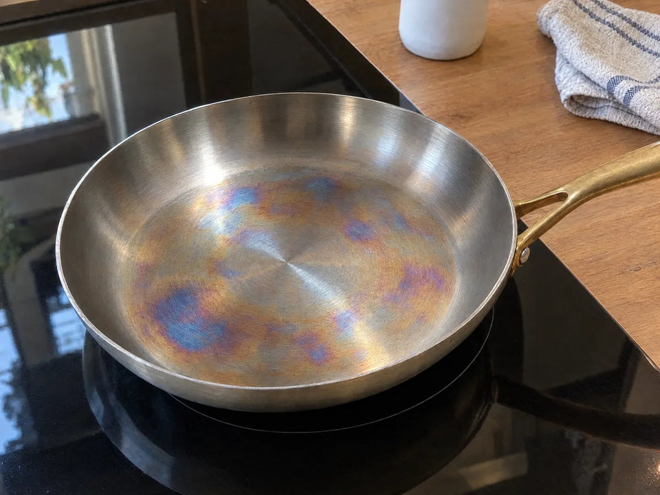 Reflets arc-en-ciel sans danger au centre de la surface de cuisson d'une poêle en inox posée sur une plaque à induction