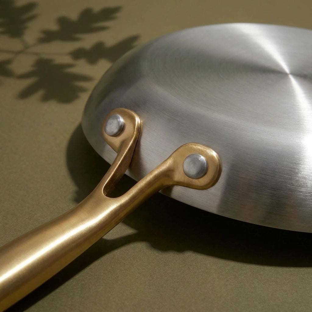 Dessous brossé de la poêle tous feux 22 cm et les deux rivets qui fixent son manche doré, vus de près