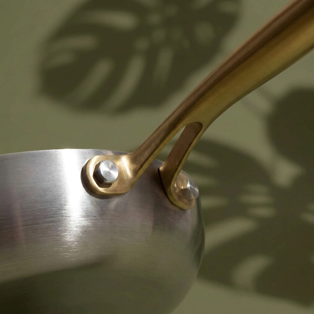 Fixation en fourche du manche doré de la poêle tous feux 22 cm, tenue par deux rivets sur la paroi