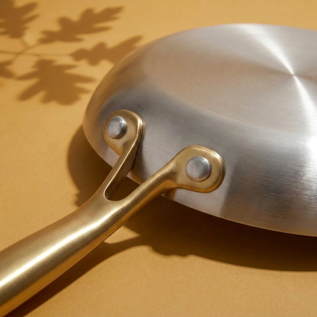 Poêle tous feux 24 cm retournée, son dessous brossé et la fourche du manche doré tenue par deux rivets