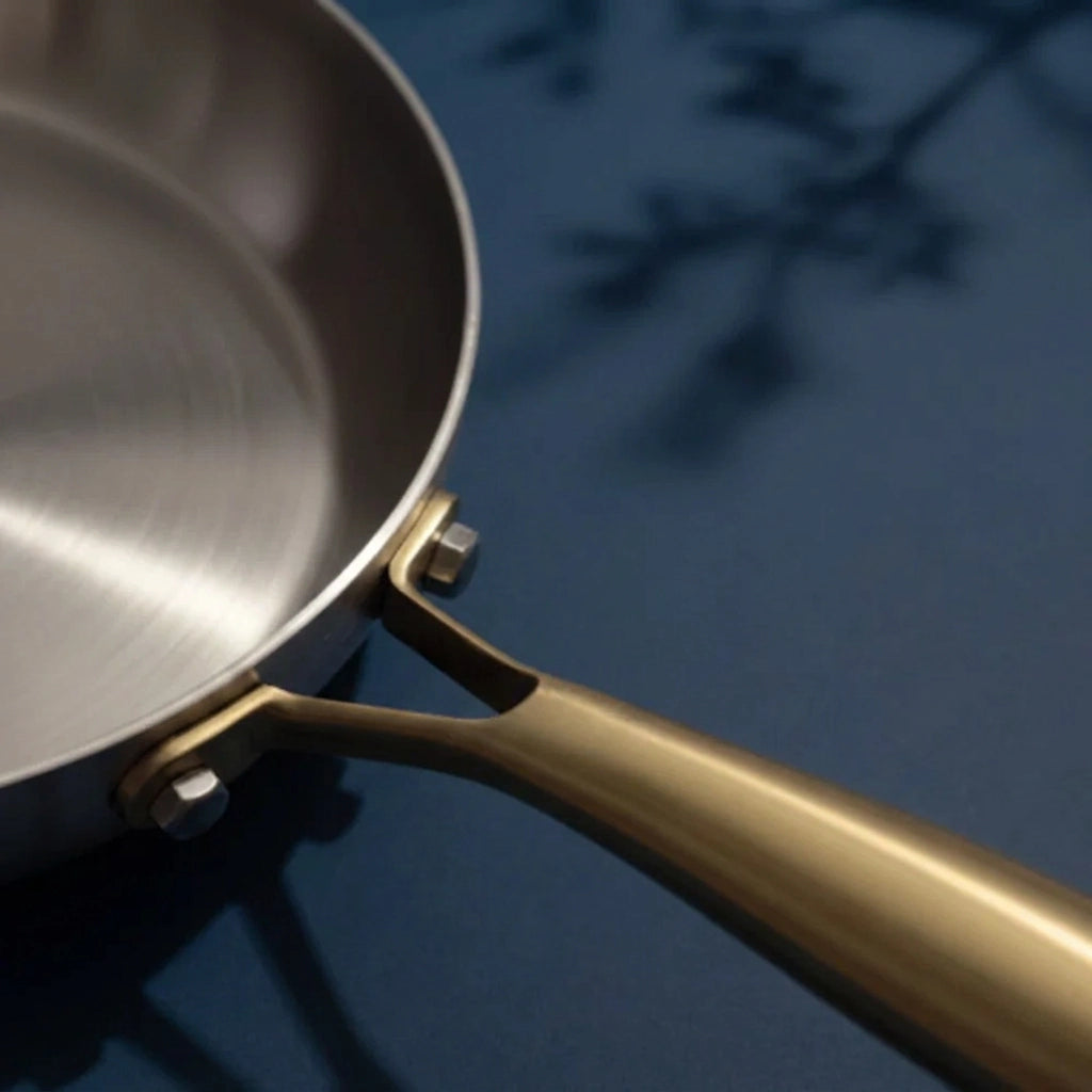 Surface de cuisson brossée de la poêle tous feux 26 cm vue d'en haut, et son manche doré fixé en fourche