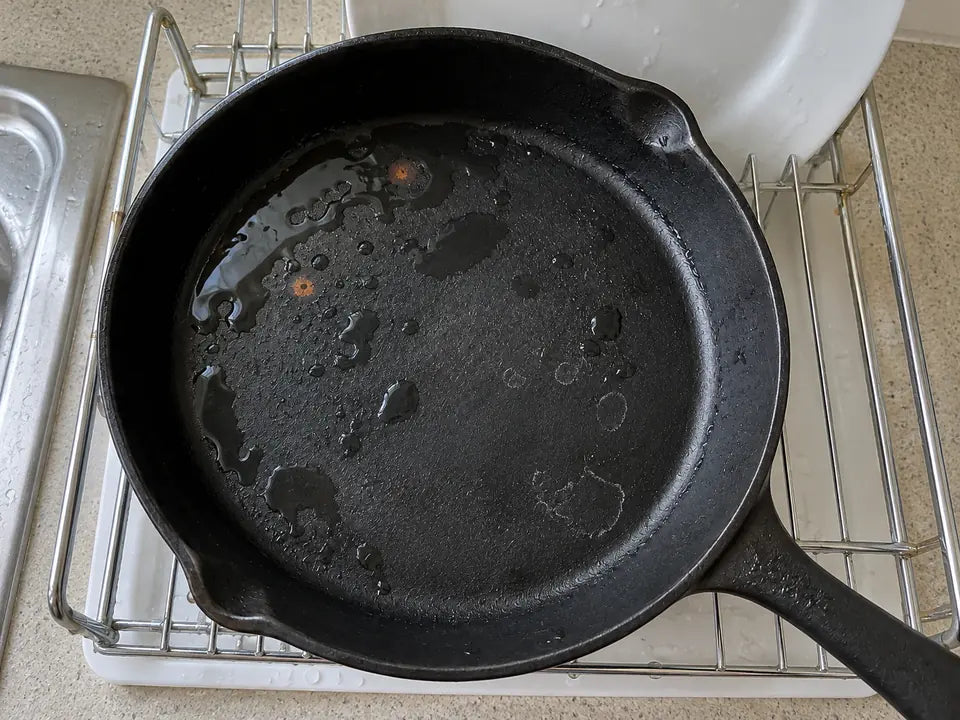 Pourquoi la fonte rouille : de l'eau restée dans une poêle en fonte posée sur un égouttoir, avec deux petites taches orange