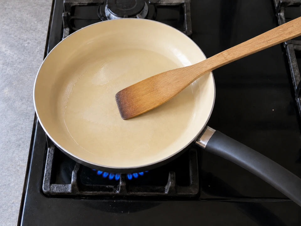 Précautions avec une poêle en céramique : un filet d'huile et une spatule en bois dans la poêle, sur une petite flamme