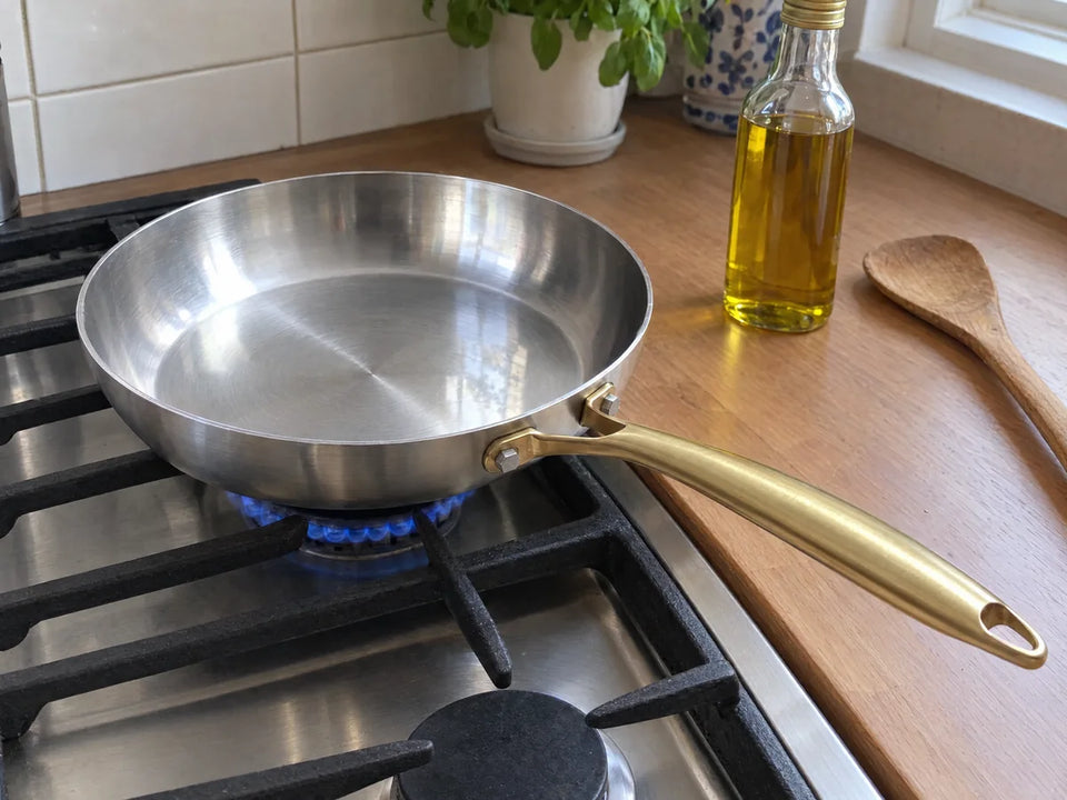 Poêle en inox qui préchauffe à vide sur le gaz, la bouteille d'huile encore fermée posée à côté