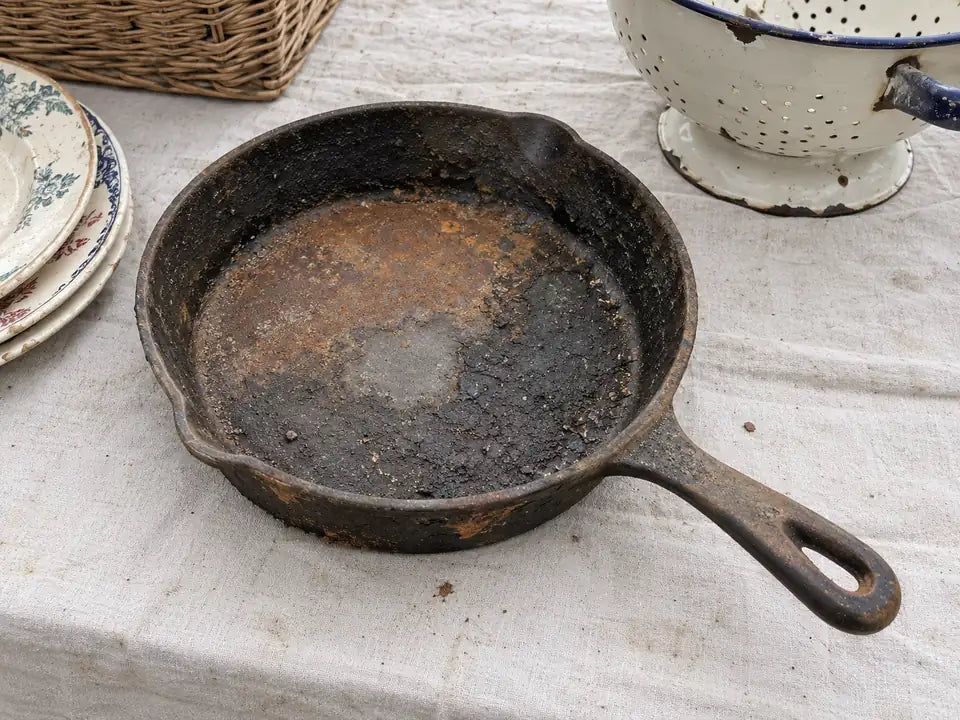 Récupérer une vieille poêle en fonte : une poêle rouillée sur un étal de brocante, entre une passoire et des assiettes