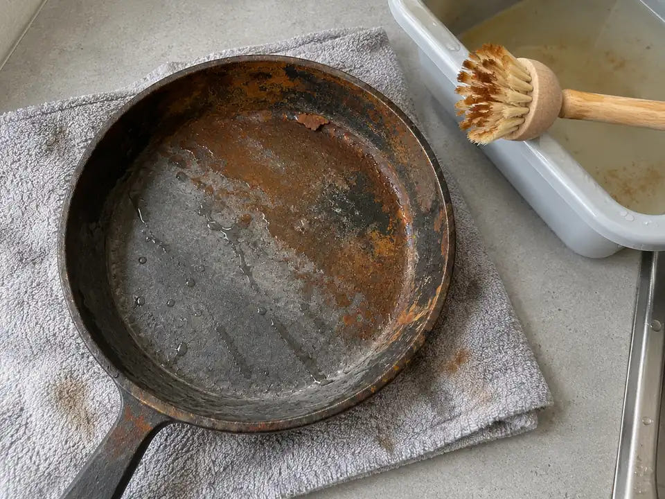 Rouille d'une poêle en fonte et bain de vinaigre blanc dilué : la poêle sortie de la bassine est à moitié brossée et la fonte grise apparaît