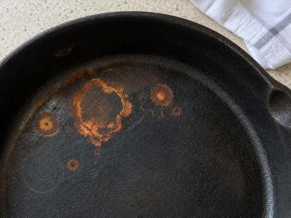 Rouille d'une poêle en fonte, est-elle toxique : une tache orange vue de près sur la surface de cuisson, torchon blanc à côté