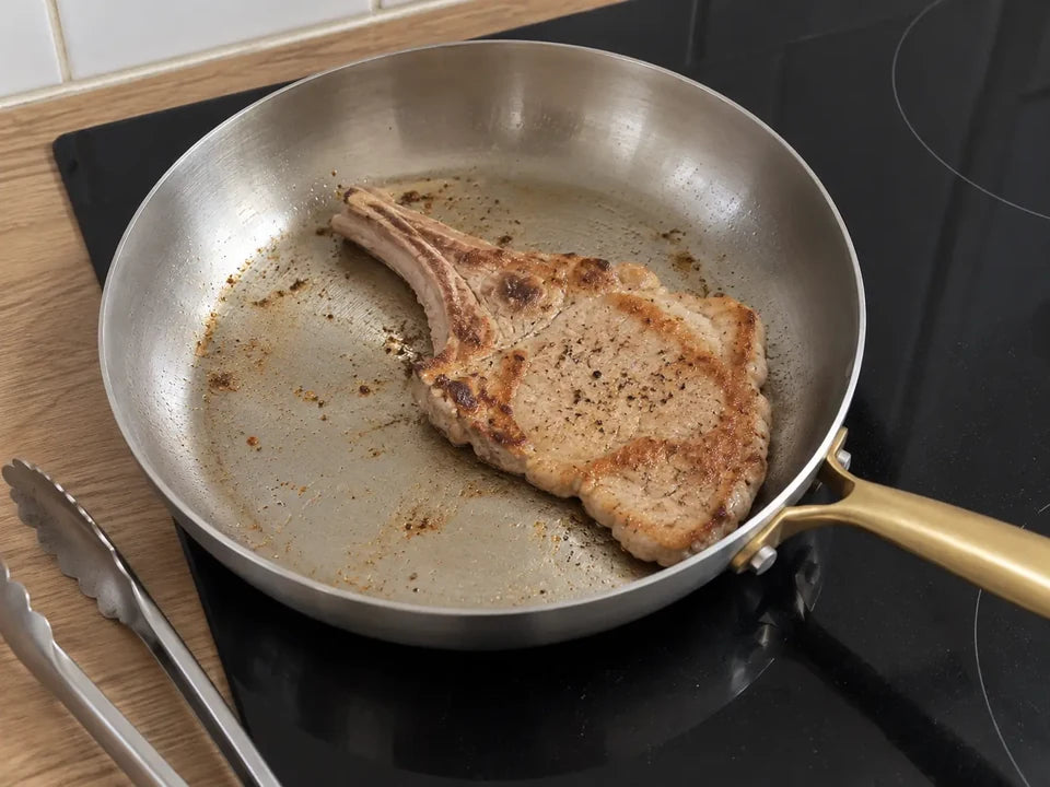 Côte de veau retournée dans une poêle en inox, sa face saisie bien dorée, une pince de cuisine posée à côté