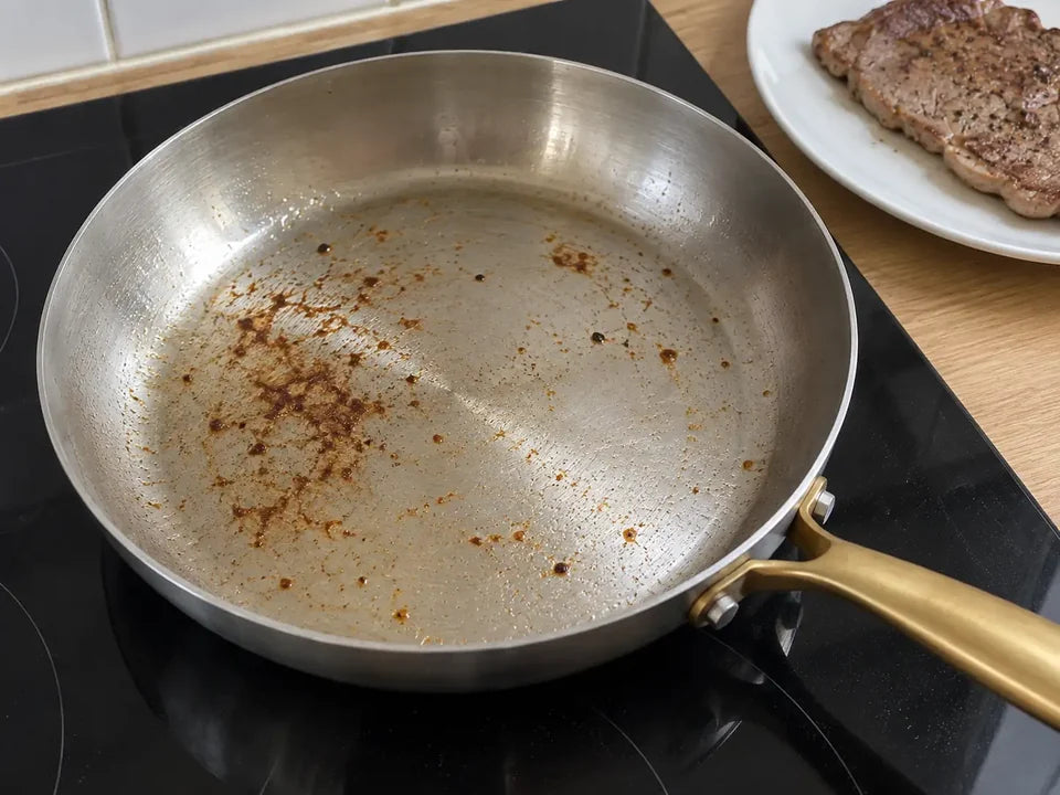 Sucs de cuisson dorés sur la surface d'une poêle en inox après la cuisson d'une viande, le steak posé sur une assiette